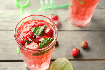 Glass with strawberry mojito on wooden table
