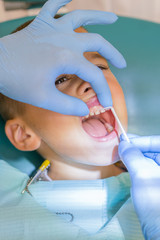 Naklejka premium Dentist examining boy's teeth in clinic. A small patient in the dental chair smiles. Dantist treats teeth. close up view of dentist treating teeth of little boy in dentist office. vertical photo.