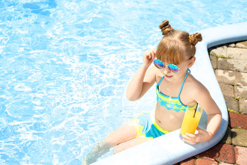 Cute little girl drinking juice in swimming pool