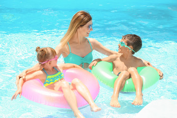 Happy mother and children with inflatable rings resting in swimming pool