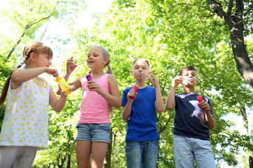 Fototapeta premium Cute little children blowing soap bubbles in park