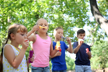 Fototapeta na wymiar Cute little children blowing soap bubbles in park