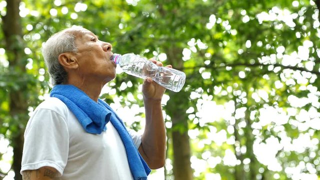 Senior man Asians drinking water from plastic bottles after jogging. He quenches thirst after fitness outdoors.  Healthy exercise lifestyle. video 4K Slow motion