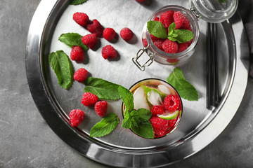 Glass of fresh raspberry mojito and jar with fresh berries on metal plate