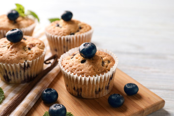Wooden board with tasty blueberry muffins on table