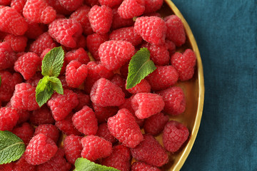 Plate with delicious fresh ripe raspberries on color cloth
