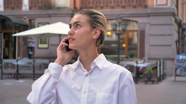 Young modern woman is standing on street and talking on phone, accepts appointment, communication concept, urban concept
