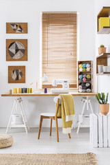 Sewing machine on a wooden desk by the window in a scandi crafts room interior with white walls and yarn. Real photo. © Photographee.eu