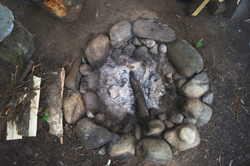 Round stone forest fireplace with coal and wood ash. Forest stand camp of hunters and tourists