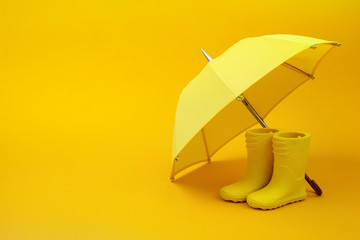A pair of yellow rain boots and a umbrella on a yellow - obrazy, fototapety, plakaty