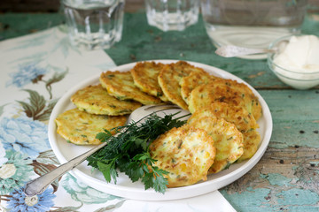 Pancakes with zucchini and sweet corn, served with sour cream, parsley and dill. Vegetarian food.