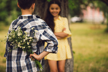 Young boy giving flowers to girl. Sweet little boy holding bouqet of flowers behind his back to give them to his little miss.