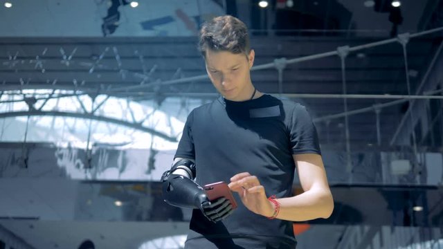 Disabled person with a cyborg arm types in his phone, looking at it. 4K.