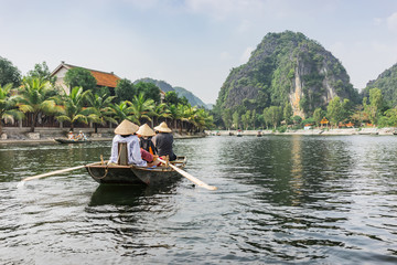 Fototapeta na wymiar Boatride from Vung Tram Pier. Traditional paddle-boat trip lets the tourists truly appreciate the serenity and beauty of nature along the Ngo Dong River, grottoes and limestone karsts Tam Coc.