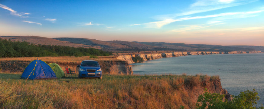 Сampground among the picturesque hills near the coast of the sea. Family is relaxing in the tent camp.
