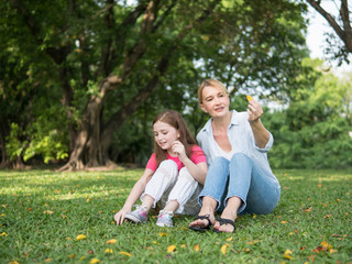 Mother and daughter sitting and playing together in the park. Happy family resting together on green grass. Happy family concept.