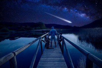 Man with dog outdoor looking at Perseid Meteor Shower and the Milky Way.
