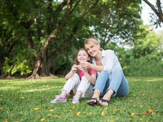 Mother and daughter sitting and playing together in the park. Happy family resting together on green grass. Happy family concept.