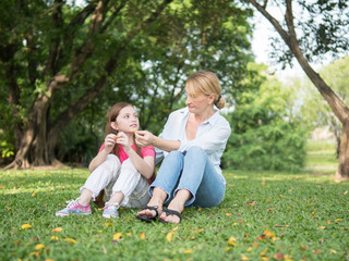 Fototapeta premium Mother and daughter sitting and playing together in the park. Happy family resting together on green grass. Happy family concept.