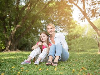 Fototapeta premium Mother and daughter sitting and playing together in the park. Happy family resting together on green grass. Happy family concept.