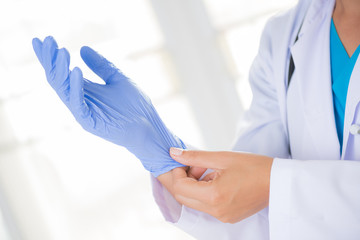 Female doctor with a stethoscope on one shoulder putting on sterile gloves. Healthcare And Medical concept.