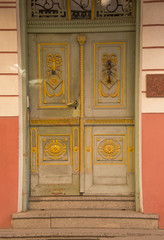 Fototapeta na wymiar Fancy old green wooden doors with yellow design. There are three stone steps leading up to doorway.