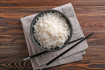 Bowl with boiled white rice and chopsticks on wooden table