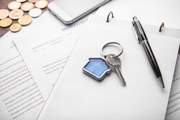 Key with trinket, notebook and documents on table. Mortgage concept