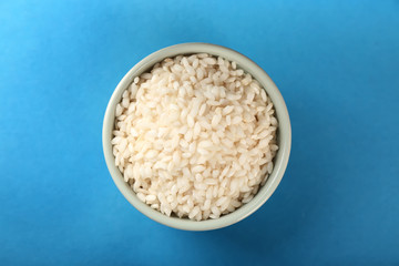 Bowl with raw rice on color background