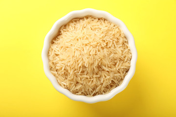 Bowl with raw brown rice on color background