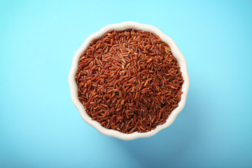 Bowl with raw red rice on color background