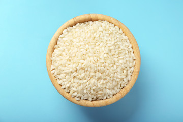 Wooden bowl with raw rice on color background