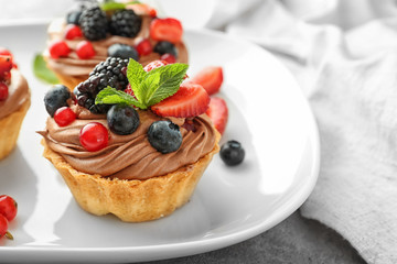 Tasty tartlets with chocolate cream and berries on plate, closeup