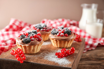 Wooden board with tasty tartlets on table