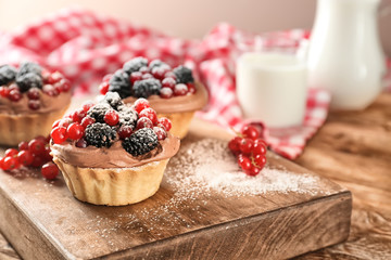 Tasty tartlets with berries on wooden board