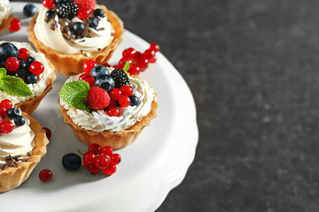 Tasty tartlets with whipped cream and berries on dessert stand, closeup