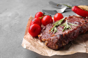 Tasty grilled meat with vegetables and herbs on grey table
