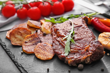 Slate plate with tasty grilled meat, vegetables and herbs on table, closeup