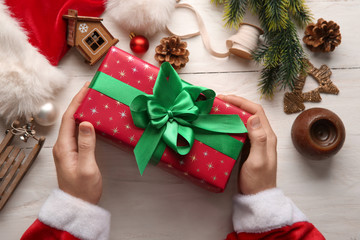 Santa Claus holding gift box on wooden table, top view