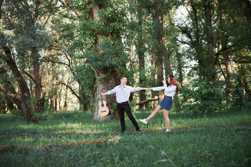 young couple walking in the forest and playing guitar, summer nature, bright sunlight, shadows and green leaves, romantic feelings