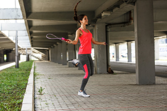 Female in sports outfit workout on the street with jump rope.