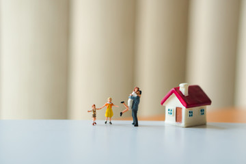Miniature people, happy family standing with mini house using as family concept