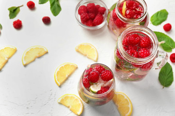 Glass and jars of fresh raspberry mojito on white table