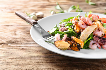 Plate of delicious vegetable salad with seafood on wooden table, closeup
