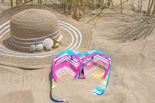 hat and summer flip-flops in beach sand