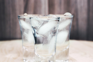 Vodka shots with ice on a wooden background