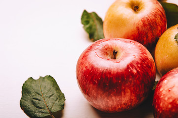 Ripe wet red and yellow apples lying in a pile with green leaves. Harvesting, autumn.