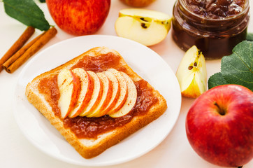 Toast with a crushed apple jam, slices of fresh apples, cinnamon on a plate on a white table. Apples and apple jam in jar. The concept.