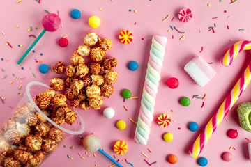 Colored, children's, unhealthy candy, marmalade, marshmallow, caramel popcorn, chupa-chups on a pink background. A table full of sweets. Top view