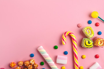 Colored, different sweets, lollipops, marshmallows, caramel popcorn on a pink background. Copy space. Top view, sweets concept